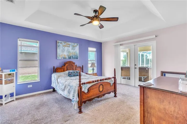 Carpeted bedroom featuring french doors, access to outside, a raised ceiling, and multiple windows