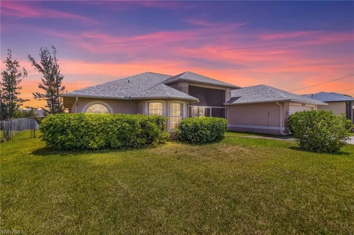 View of front of property featuring a front lawn, an attached garage, fence, stucco siding, and a sunroom