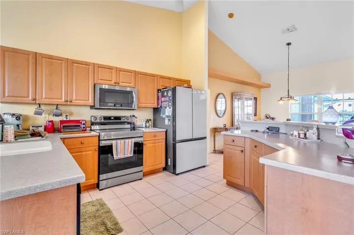 Kitchen featuring high vaulted ceiling, light brown cabinets, a sink, light countertops, and appliances with stainless steel finishes