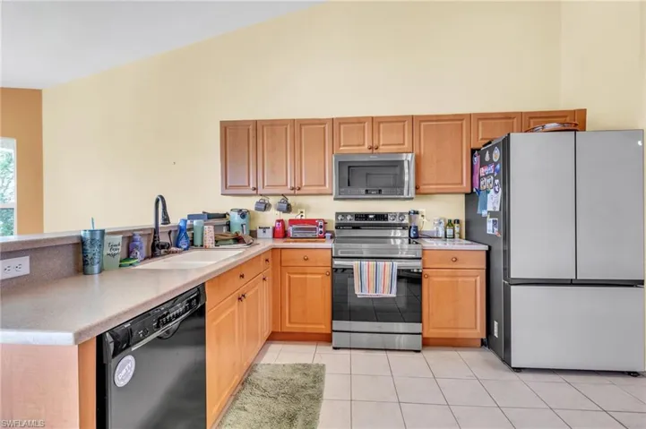 Kitchen featuring stainless steel appliances, a peninsula, a sink, light tile patterned flooring, and light countertops