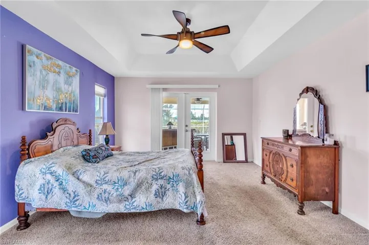 Bedroom featuring light carpet, french doors, a tray ceiling, and baseboards