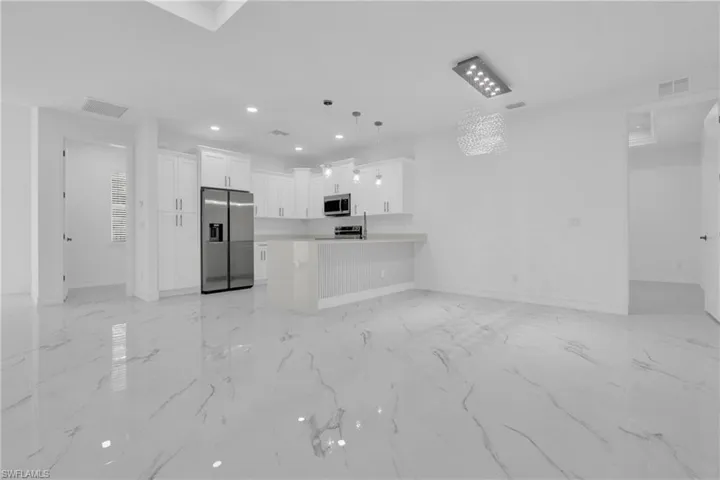 Kitchen with open floor plan, white cabinets, light countertops, stainless steel appliances, and pendant lighting
