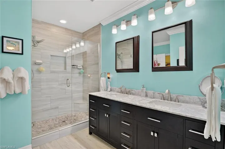 Bathroom with double vanity, light wood-type flooring, a shower stall, and crown molding