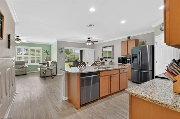Kitchen featuring light stone counters, ornamental molding, stainless steel appliances, open floor plan, and a kitchen island with sink