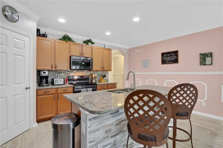 Kitchen with arched walkways, light stone counters, a kitchen bar, an island with sink, and decorative backsplash