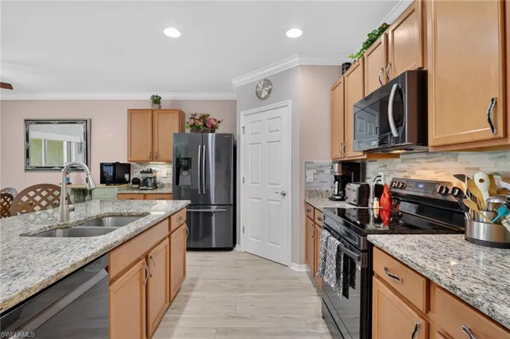 Kitchen with black appliances, light stone countertops, ornamental molding, backsplash, and recessed lighting