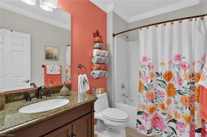Bathroom with crown molding, shower / bathtub combination with curtain, vanity, and light wood-style floors
