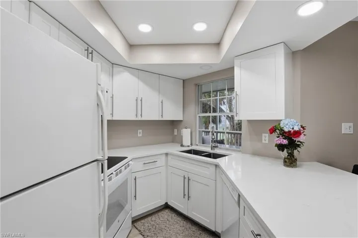 Kitchen with white appliances, white cabinets, recessed lighting, light stone countertops, and a raised ceiling