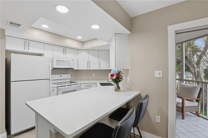 Kitchen featuring white appliances, white cabinetry, a kitchen breakfast bar, a peninsula, and recessed lighting