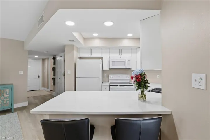 Kitchen featuring white appliances, a peninsula, a kitchen bar, recessed lighting, and white cabinets