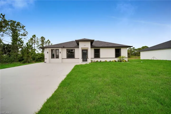 Contemporary stucco exterior with dark trim accents, a dark shingled roof, a large concrete driveway, a prominent front door, and a landscaped front yard