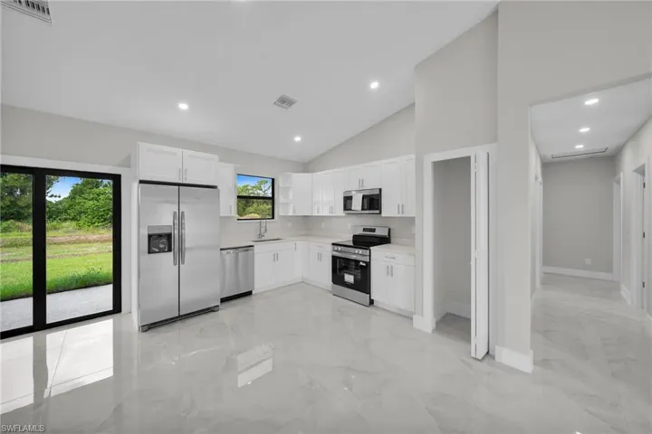 Modern kitchen featuring white cabinetry, stainless steel appliances, light countertops, and large format tile flooring