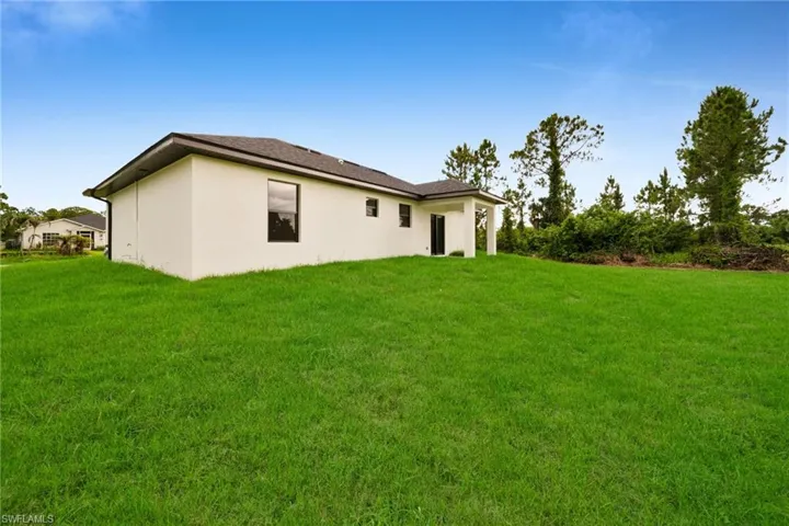 Expansive green lawn bordering a single-story residence with a stucco exterior, dark-framed windows, and a covered patio area