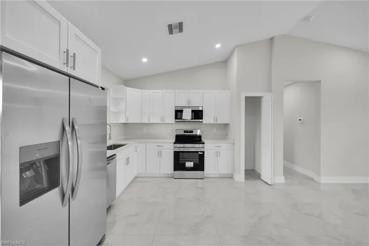 Modern kitchen featuring white shaker cabinetry with brushed nickel hardware, stainless steel appliances, light-toned countertops, and a full backsplash