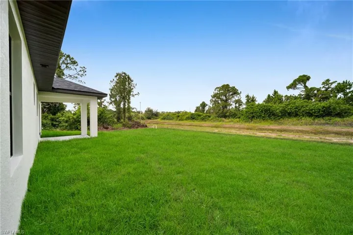 Expansive green lawn extending from the residence, featuring a covered patio with white columns and a dark shingle roof