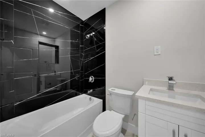 Bathroom featuring striking black tiled shower surround with white veining, white bathtub, contemporary vanity with light-toned countertop, integrated sink, and modern chrome faucet