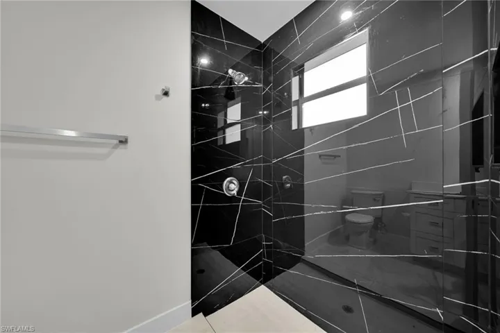 Shower enclosure featuring black polished wall tile with white veining, polished chrome fixtures, and a clear glass partition