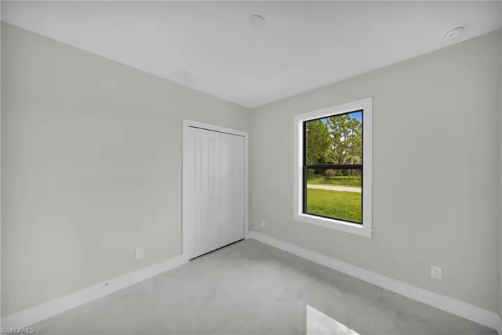 Bright interior space featuring a window with white trim, a bi-fold closet, light gray walls, white baseboards, and large format gray floor tiling