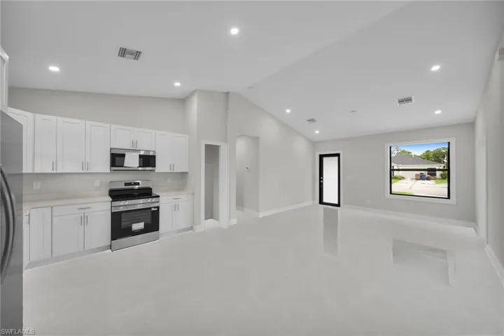 Open-concept living space with a contemporary kitchen featuring white cabinetry, light countertops, and stainless steel appliances