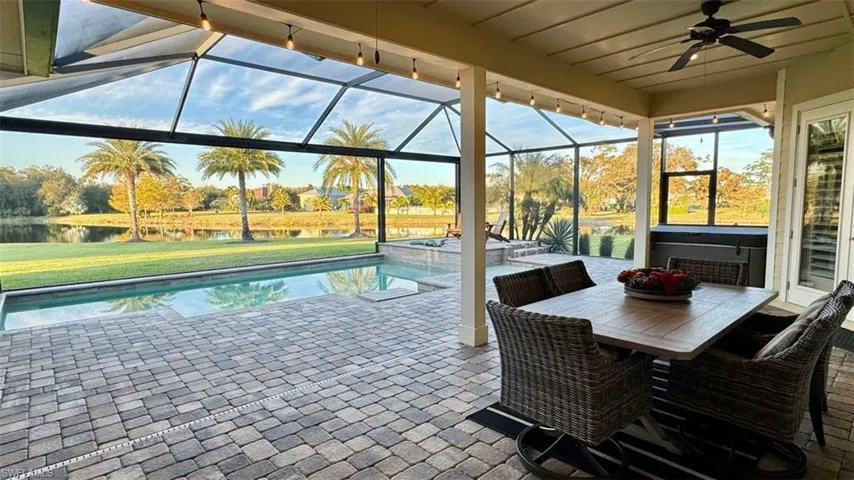 View of pool with glass enclosure, ceiling fan, a yard, a patio area, and a water view