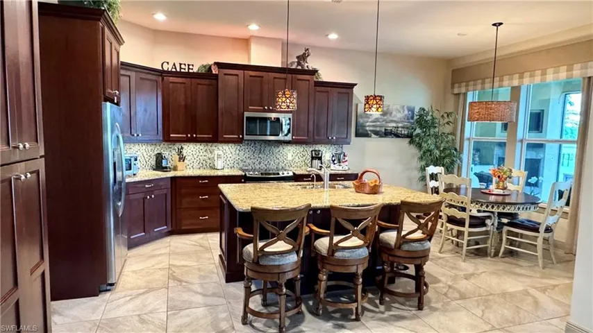 Kitchen featuring light stone counters, stainless steel appliances, sink, decorative light fixtures, and an island with sink