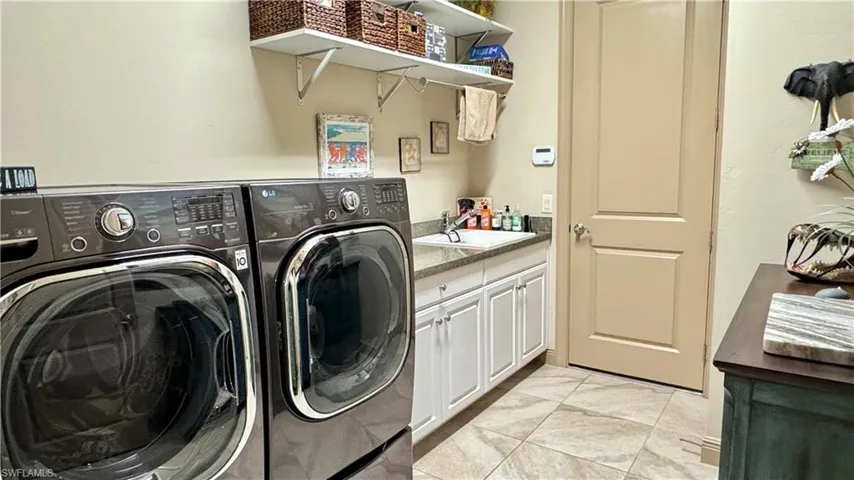 Laundry area with washer and dryer, light tile patterned floors, cabinets, and sink