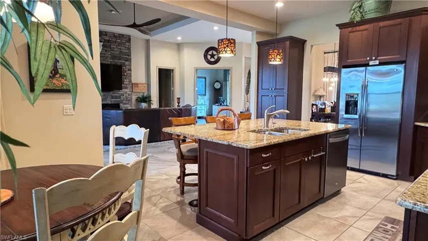 Kitchen featuring appliances with stainless steel finishes, sink, light tile patterned floors, decorative light fixtures, and an island with sink