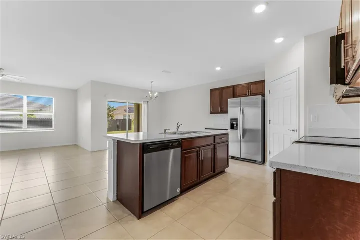 Kitchen featuring stainless steel appliances, light countertops, a kitchen island with sink, a chandelier, and hanging light fixtures