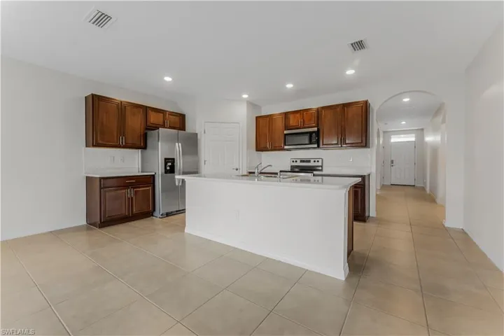 Kitchen featuring stainless steel appliances, decorative backsplash, arched walkways, light countertops, and light tile patterned floors