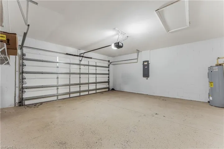Garage with electric panel, water heater, a garage door opener, and concrete block wall
