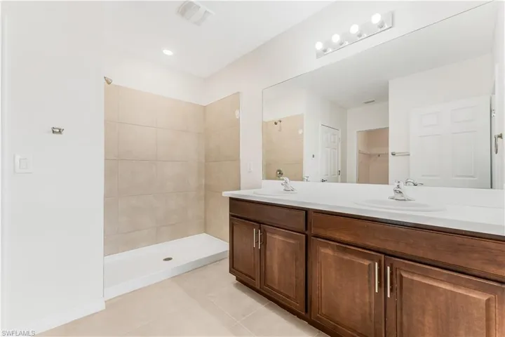 Full bath featuring tile patterned floors, double vanity, a tile shower, and a spacious closet