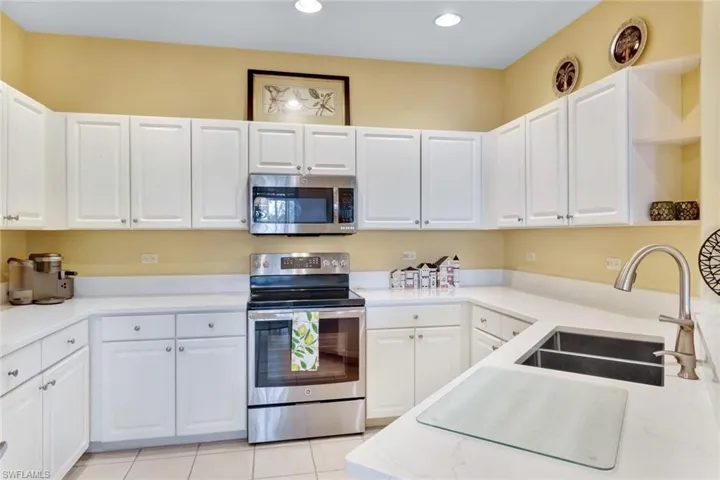 Kitchen with sink, white cabinets, light tile patterned floors, and appliances with stainless steel finishes