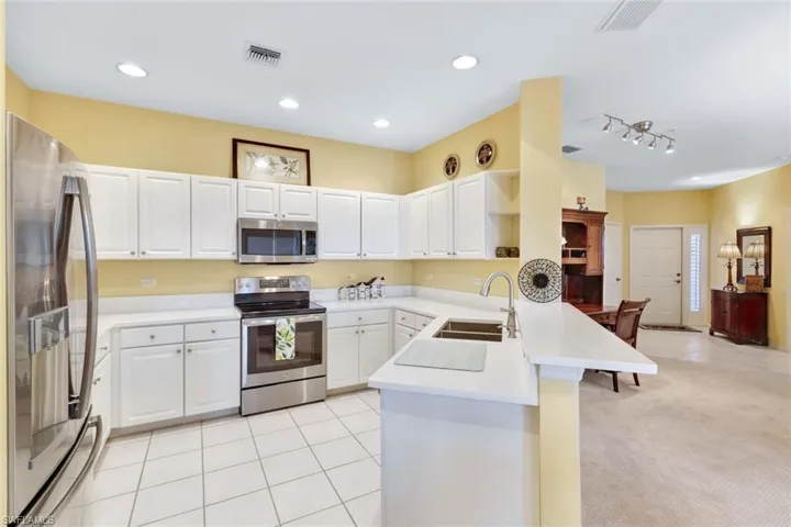 Kitchen with white cabinetry, sink, kitchen peninsula, light carpet, and appliances with stainless steel finishes
