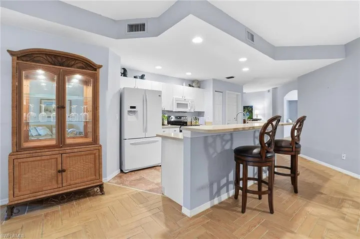 Kitchen featuring white appliances, a kitchen breakfast bar, arched walkways, an island with sink, and white cabinetry