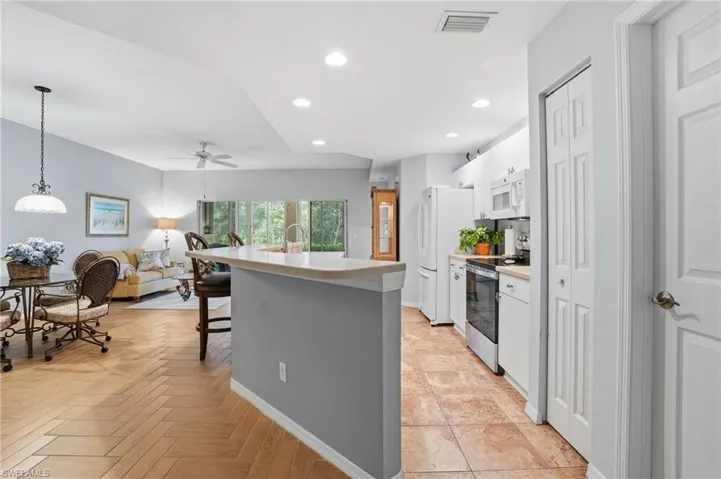 Kitchen featuring light countertops, white appliances, a center island with sink, recessed lighting, and a breakfast bar