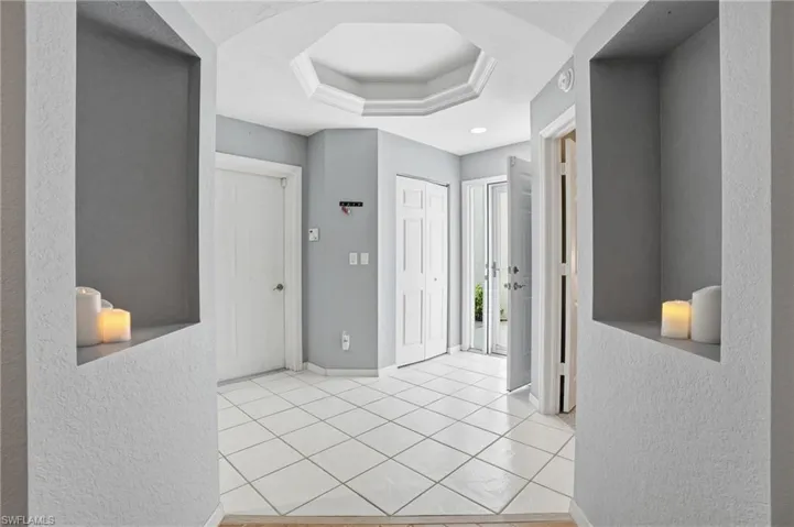 Hallway with a textured wall, a raised ceiling, and light tile patterned floors