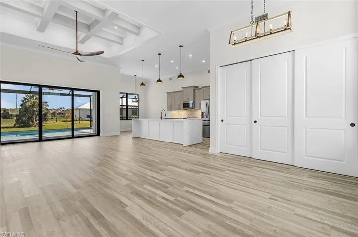 Unfurnished living room featuring sink, ceiling fan with notable chandelier, coffered ceiling, beam ceiling, and light hardwood / wood-style flooring