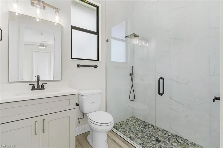 Bathroom with ceiling fan, hardwood / wood-style flooring, toilet, a shower with shower door, and vanity
