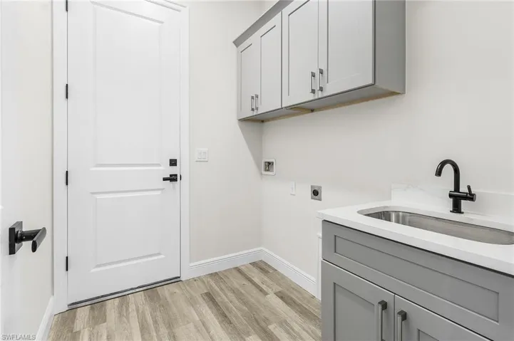 Washroom with hookup for a washing machine, hookup for an electric dryer, sink, cabinets, and light hardwood / wood-style flooring