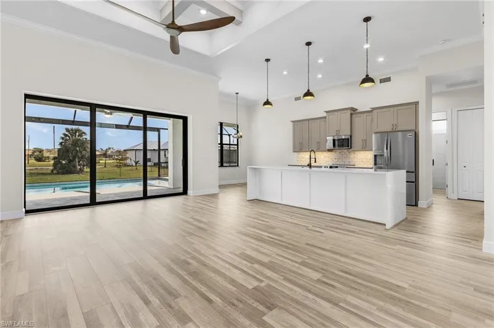 Kitchen featuring appliances with stainless steel finishes, an island with sink, light hardwood / wood-style floors, decorative light fixtures, and gray cabinets