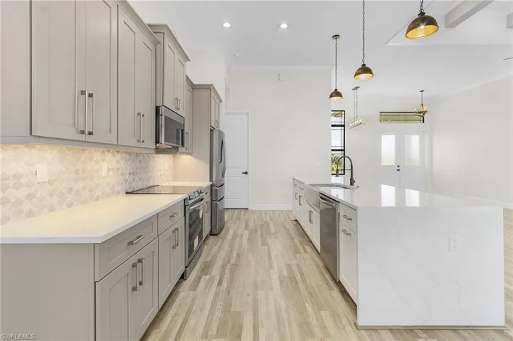 Kitchen with stainless steel appliances, sink, gray cabinetry, crown molding, and decorative light fixtures