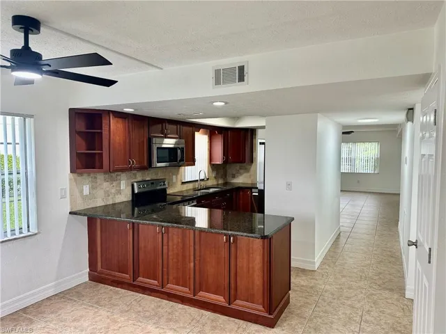Kitchen featuring tasteful backsplash, dark stone countertops, kitchen peninsula, sink, and range with electric cooktop