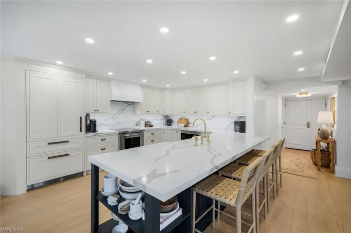 Kitchen featuring white cabinets, a peninsula, light stone counters, a breakfast bar area, and decorative backsplash