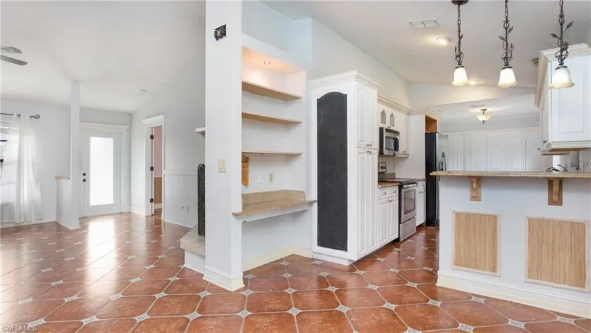 Kitchen featuring patterned tile flooring, breakfast bar, hanging light fixtures, white cabinetry and stainless steel finish appliances