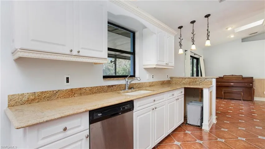 Kitchen featuring stainless steel finish dishwasher, pendant lighting, granite counters, white cabinets and  patterned tile flooring