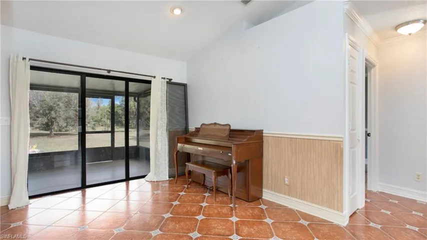 Living room featuring patterned tile flooring, chair rail, crown molding, vaulted ceiling and sliding glass door to the covered lanai