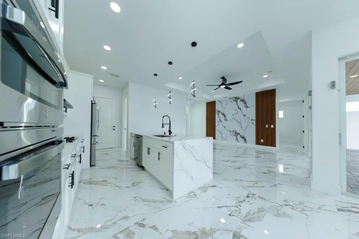 Kitchen with white cabinetry, stainless steel appliances, light stone counters, pendant lighting, and open floor plan