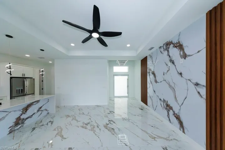 Unfurnished living room with light marble finish floors, recessed lighting, a tray ceiling, stone wall, and a ceiling fan