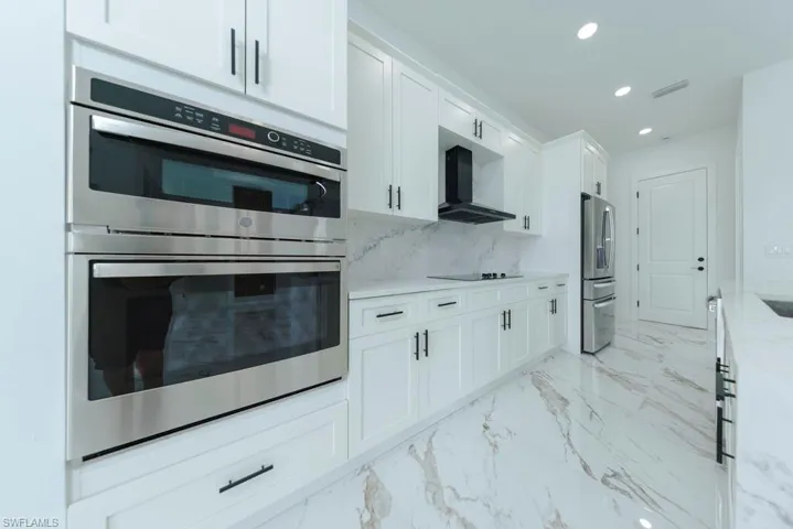Kitchen featuring appliances with stainless steel finishes, recessed lighting, light marble finish floors, white cabinets, and light stone countertops