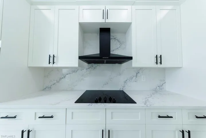 Kitchen with wall chimney exhaust hood, white cabinetry, backsplash, and light stone counters